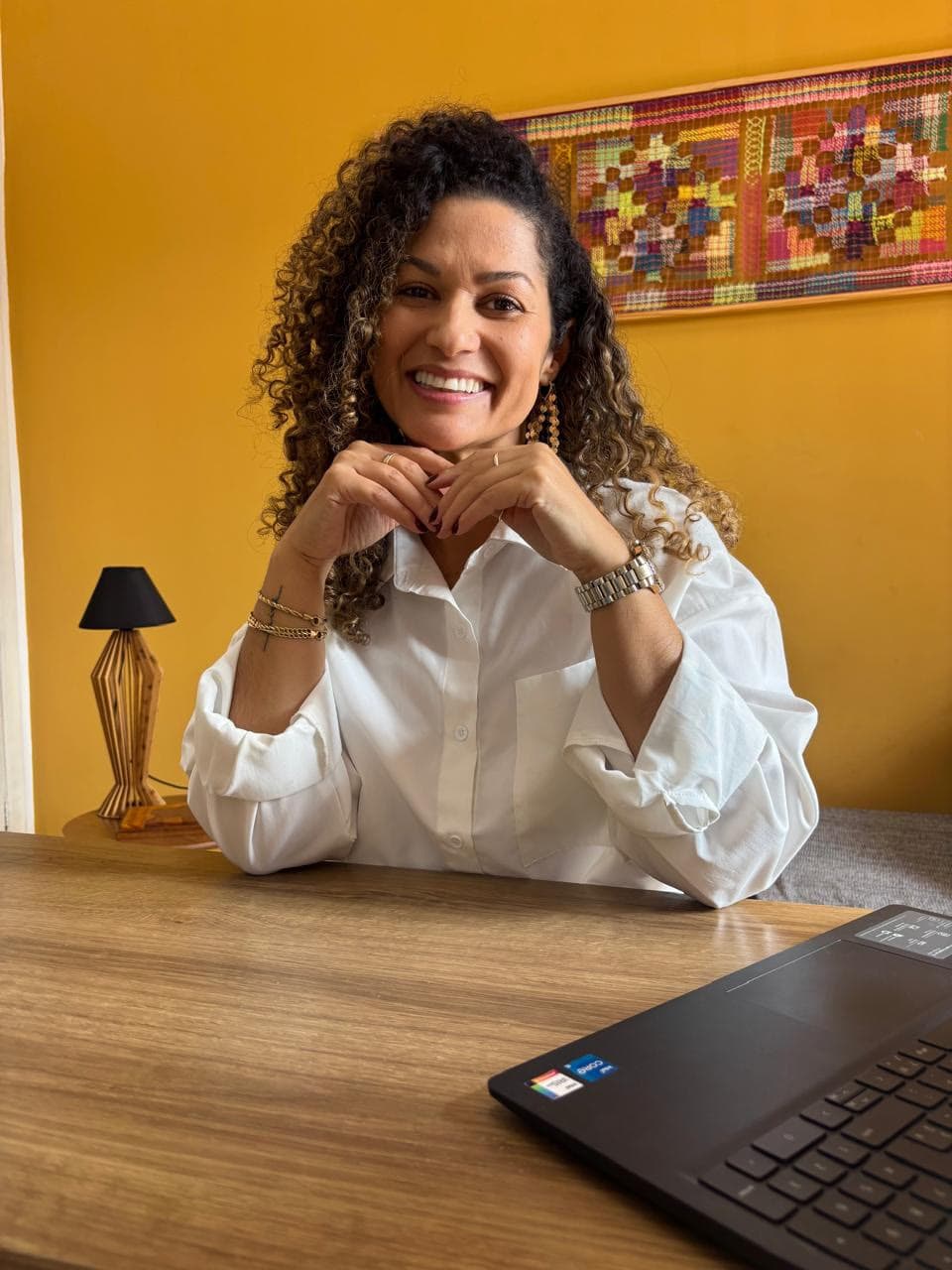 Karla França sorrindo em sua mesa de trabalho, em frente ao notebook